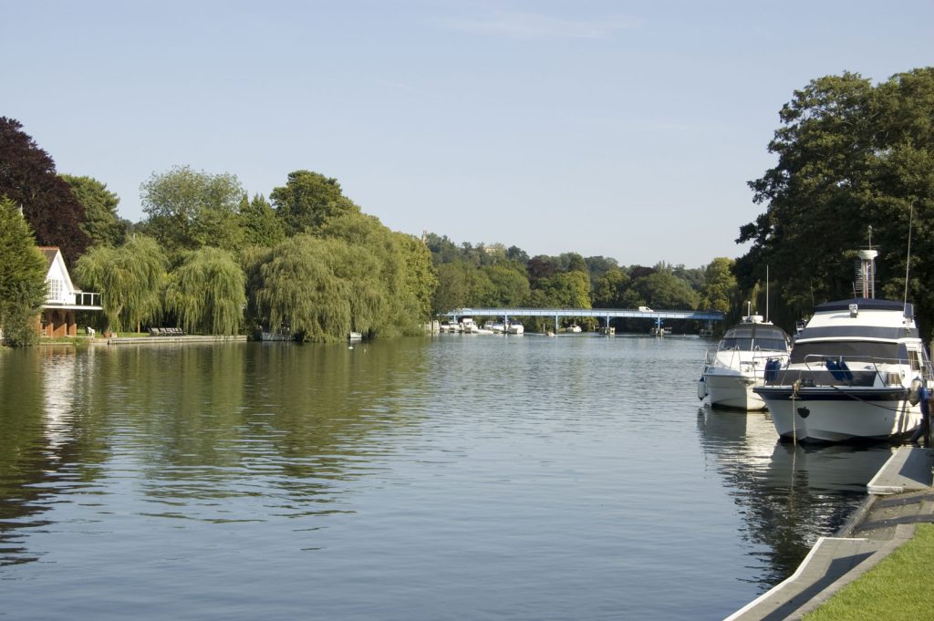 View of the Thames from Cookham village, boats on the side and bridge over river in the distance.